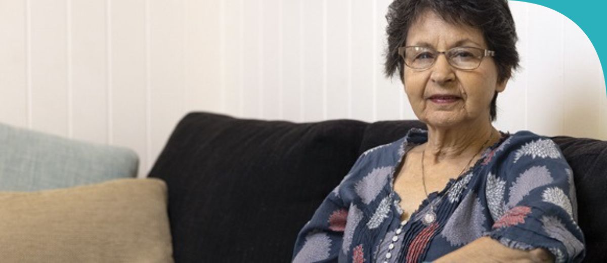 An older woman sits on a couch and looks at the camera.